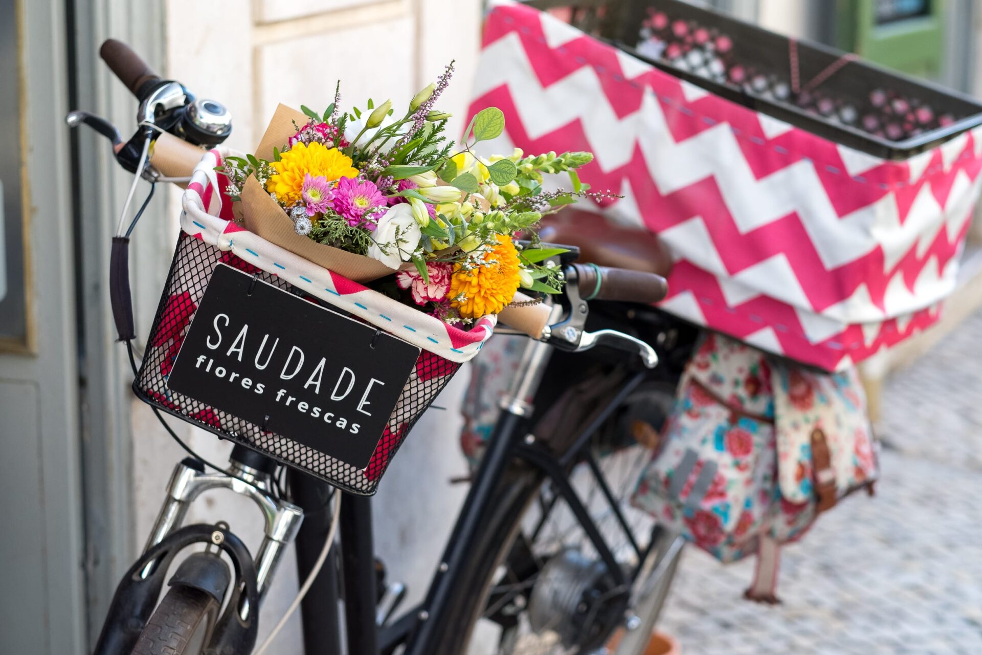 Bicicleta com cesto cheio de flores coloridas e placa Saudade Flores frescas numa rua de Lisboa
